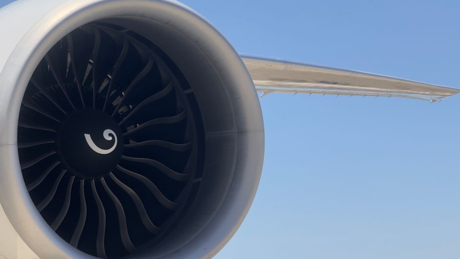 Detailed view of an aircraft jet engine with turbine blades against a clear blue sky.