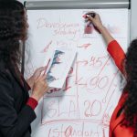 GAI Strategy: How to Prepare Your Business for AI Autonomy Two professional women discuss and strategize on business development in a modern office setting.