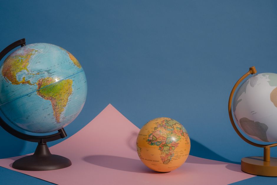 Three vividly colored globes displayed against a blue and pink backdrop, highlighting geography and education.