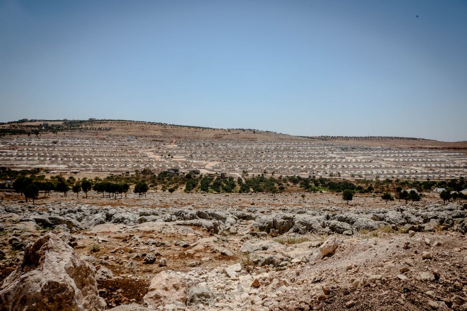Expansive view of a refugee camp amidst a dry and rocky landscape in Idlib, Syria.