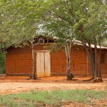 A traditional earthen house stands peacefully amid trees and greenery, showcasing rustic charm.