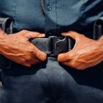 Close-up of a police officer adjusting their duty belt, highlighting law enforcement gear.