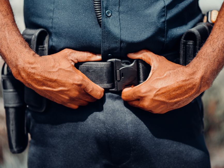 Close-up of a police officer adjusting their duty belt, highlighting law enforcement gear.