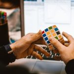 Close-up of hands solving a Rubik's Cube in front of a laptop showcasing a relaxed work environment.