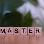 Close-up of wooden Scrabble tiles spelling the word 'MASTER' on a wooden table with a blurred background.