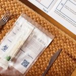 A COVID-19 test kit arranged on a woven table mat beside cutlery, highlighting healthcare at home.