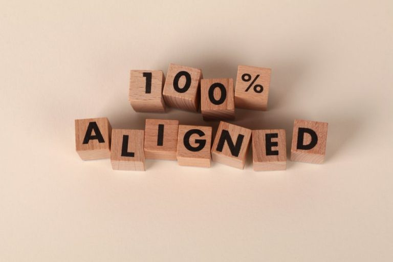 Wooden blocks spelling '100% Aligned' on a neutral background, conveying precision and alignment.
