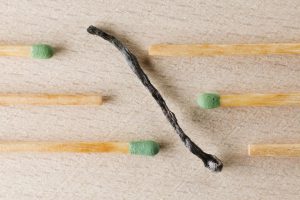 Charred match surrounded by green-tipped matches symbolizing burnout and contrast.