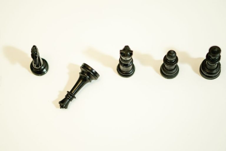 Overhead shot of black chess pieces on a white surface, symbolizing strategy and intellect.
