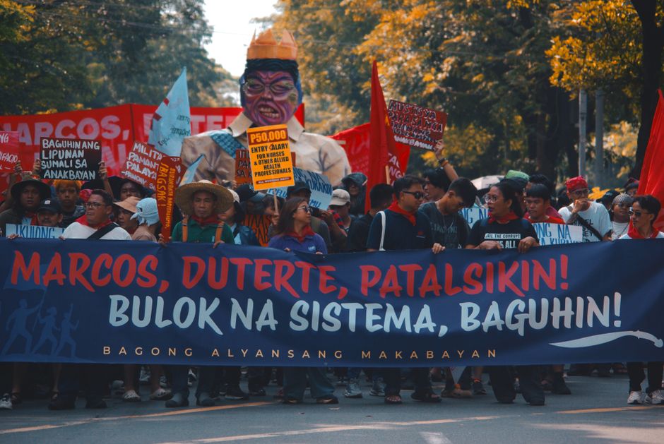 Street protest with demonstrators holding political banners and signs demanding change.