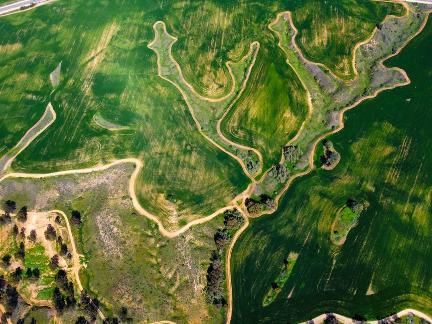 Stunning aerial view of lush green fields and winding paths in a countryside landscape.