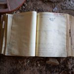An open ledger book on a dusty floor, evoking a sense of history and abandonment.
