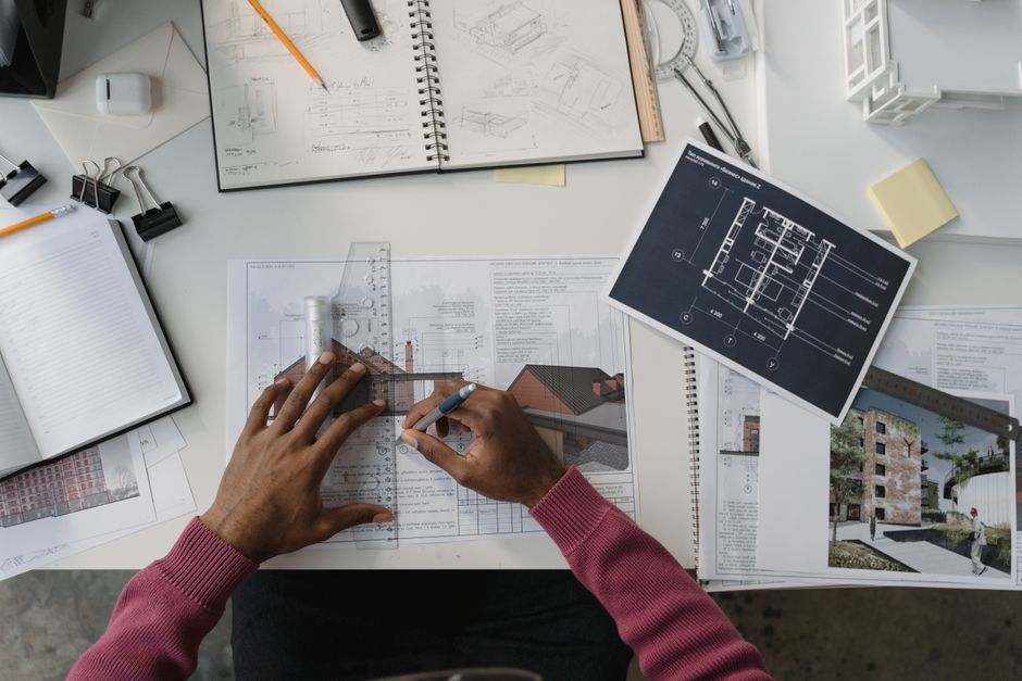 Architect designing plans at a desk surrounded by tools, drafts, and blueprints.