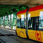 Infrastructure Inertia: Why Transit Efficiency Drives Business Modern yellow tram traversing an urban green steel bridge, showcasing urban transit infrastructure.