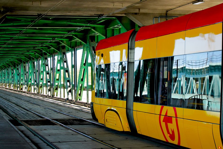 Modern yellow tram traversing an urban green steel bridge, showcasing urban transit infrastructure.