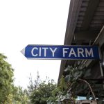 Integrated Urban Agriculture: Building Resilient City Systems A blue directional street sign pointing to a city farm, surrounded by greenery and urban elements.
