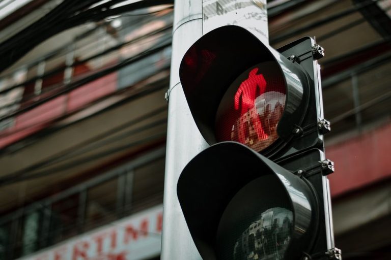Close-up of a red pedestrian traffic light against a city background, capturing urban life.