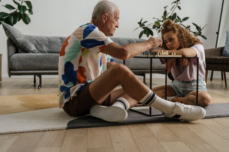 Elderly man and young girl deeply focused on a chess game in a cozy living room setting.