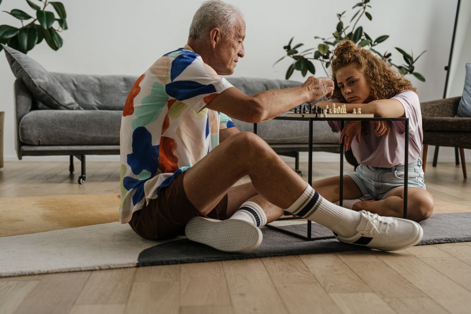 Elderly man and young girl deeply focused on a chess game in a cozy living room setting.