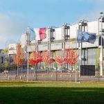 International Law as Corporate Strategy: A Leader's Guide Modern building in Compiègne, France with French and EU flags, autumn trees.