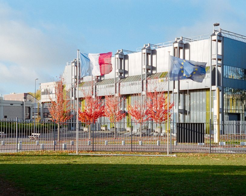 Modern building in Compiègne, France with French and EU flags, autumn trees.