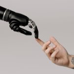 Intra-body Micro-robotics: The Future of Operational Strategy A human hand with tattoos reaching out to a robotic hand on a white background.