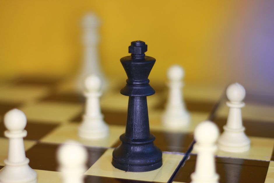A focused shot of a black king chess piece surrounded by white pawns on a chessboard.