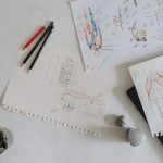 <title>Kylian Mbappé: The Anatomy of High-Stakes Execution</title> Top view of anatomical sketches with drawing tools on a desk, showcasing artistic process.