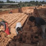 Labor Economics Lessons: From 11th Century to Modern Strategy Workers handling bricks in an outdoor factory setting, illustrating manual labor in manufacturing.
