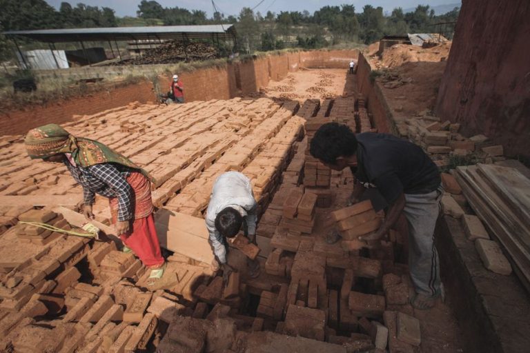 Workers handling bricks in an outdoor factory setting, illustrating manual labor in manufacturing.