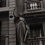 A black and white image of Lady Justice statue against a building facade symbolizing law and fairness.