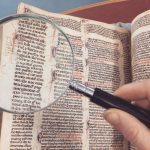 Lessons from the Magna Carta: Leadership and System Strategy A hand holding a magnifying glass over an antique book page, revealing intricate text and design.