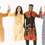 A joyful group of adults from diverse backgrounds high-fiving in traditional clothing.