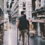 Logistics Optimization Algorithms: Scaling High-Performance Ops Two men maneuver a trolley in a large warehouse filled with boxes and shelves.