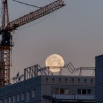 Lunar Base Construction: Operational Excellence in Space Moonrise over cityscape with construction crane and buildings.