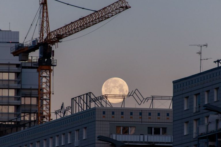 Moonrise over cityscape with construction crane and buildings.