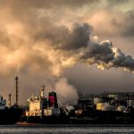 A dramatic capture of smokestacks releasing emissions over a waterfront, highlighting industrial pollution.