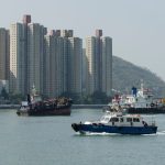 Vibrant harbor scene with skyscrapers, boats, and hills in New Territories, Hong Kong.