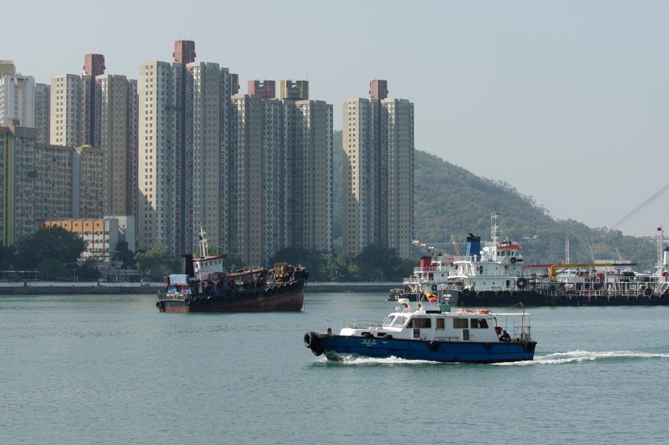Vibrant harbor scene with skyscrapers, boats, and hills in New Territories, Hong Kong.