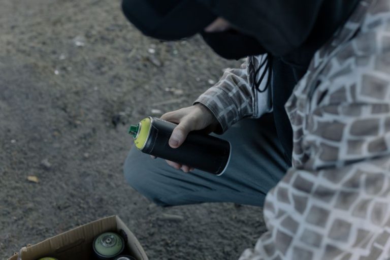 A graffiti artist holding a spray paint can outdoors, preparing to create street art.