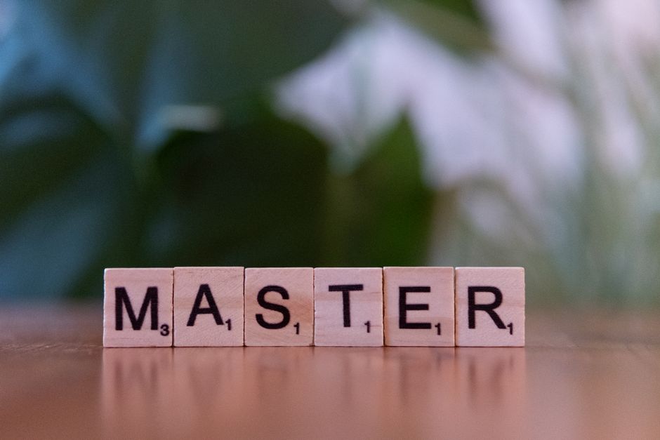 Close-up of wooden Scrabble tiles spelling the word 'MASTER' on a wooden table with a blurred background.
