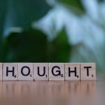 Wooden blocks spelling 'THOUGHT' on a table with a blurred background, conveying ideas and introspection.
