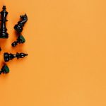 Scattered black chess pieces on an orange background, perfect for strategy concepts.