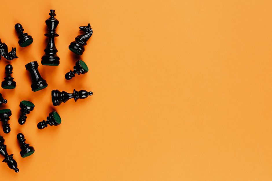 Scattered black chess pieces on an orange background, perfect for strategy concepts.