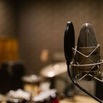 Close-up of a condenser microphone with a pop filter in a recording studio setting.