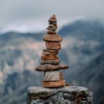 Balanced stones forming a cairn against a tranquil mountain backdrop under a cloudy sky.