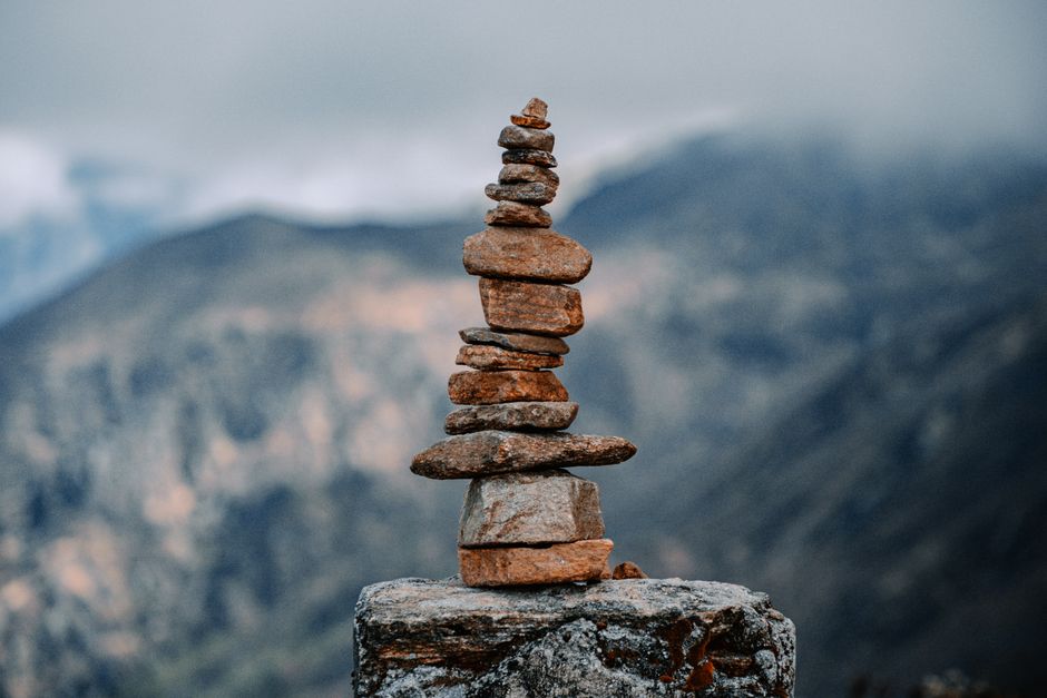 Balanced stones forming a cairn against a tranquil mountain backdrop under a cloudy sky.