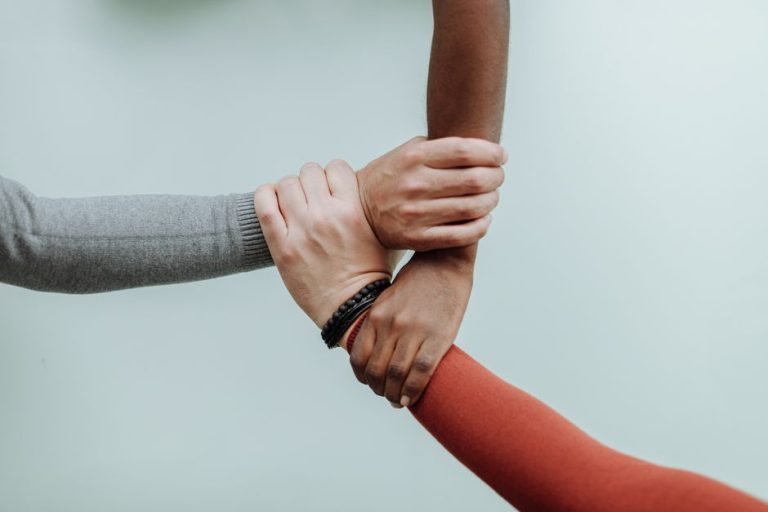 Three individuals' hands connected in a symbol of teamwork and diversity.