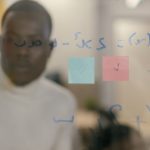 Business professional reviewing sticky notes and equations on a glass board. Problem-solving and creativity concept.