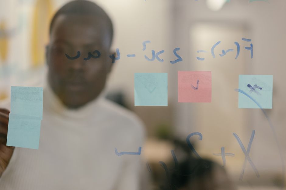 Business professional reviewing sticky notes and equations on a glass board. Problem-solving and creativity concept.
